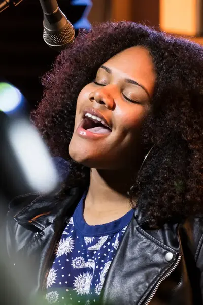 Student zingt vol expressie in een microfoon tijdens een studiosessie.