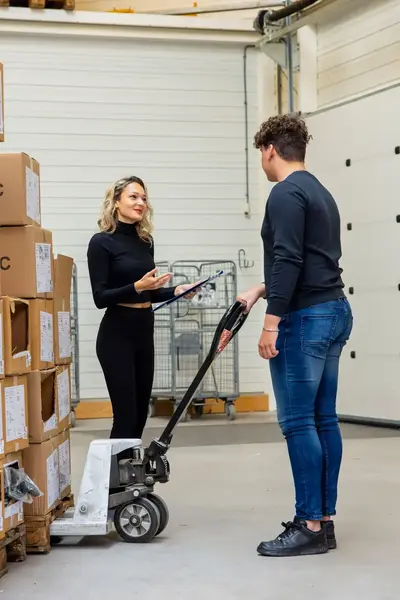 Studenten bespreken logistieke taken in een magazijn tussen stapels dozen.