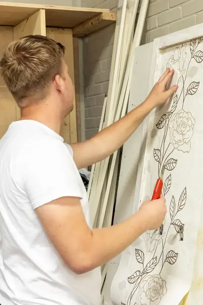Man is een print van bloemen aan het uitsnijden om als mal te kunnen gebruiken voor bijv. schilderwerk.