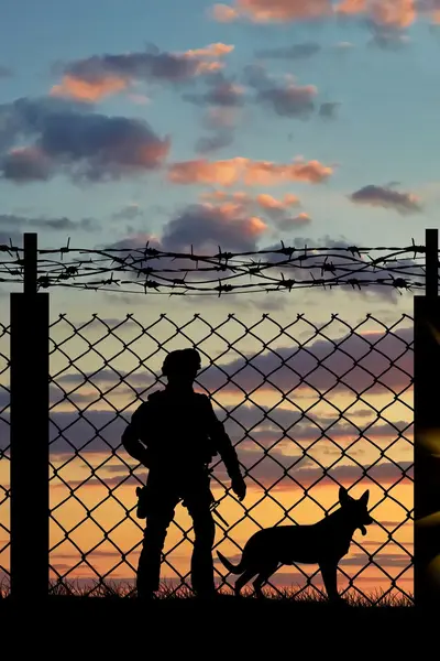 Soldaat met herdershond naast hek bij zonsondergang