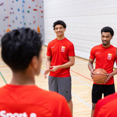 Sportstudenten in rood sporttenue in gymzaal tijdens basketbaltraining