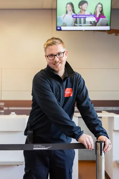 Vriendelijke beveiligingsmedewerker bij luchthaven opent een afzetlint bij de ingang van een balie.