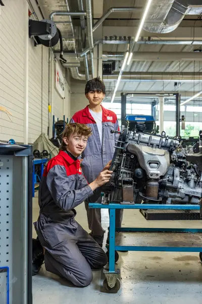Twee studenten in ROCvA-overall sleutelen aan motorblok in garage