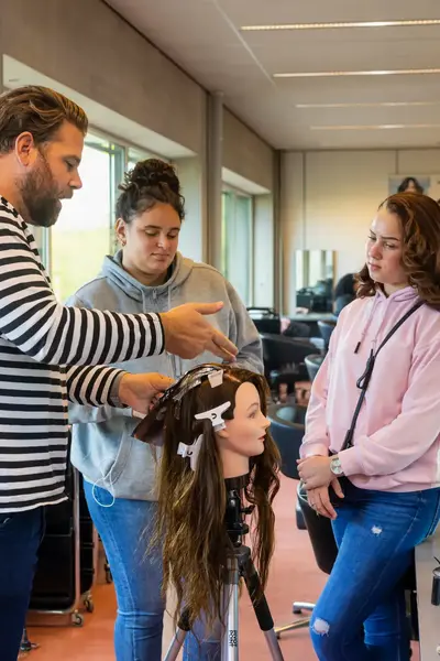 Studenten oefenen haarverzorging onder begeleiding in de salonschool.