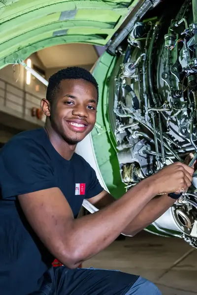 Lachende technicus werkt aan een vliegtuigonderdeel in een hangar tijdens onderhoud of reparatie.